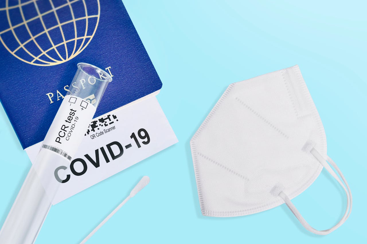 A passport, COVID-19 test, and mask against a blue background symbolizing travel safety during the pandemic.