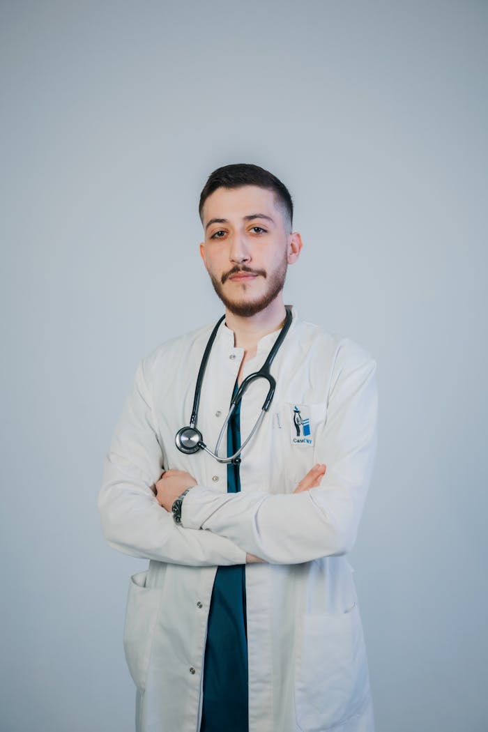Young male doctor in a white coat with crossed arms, looking confident and professional.