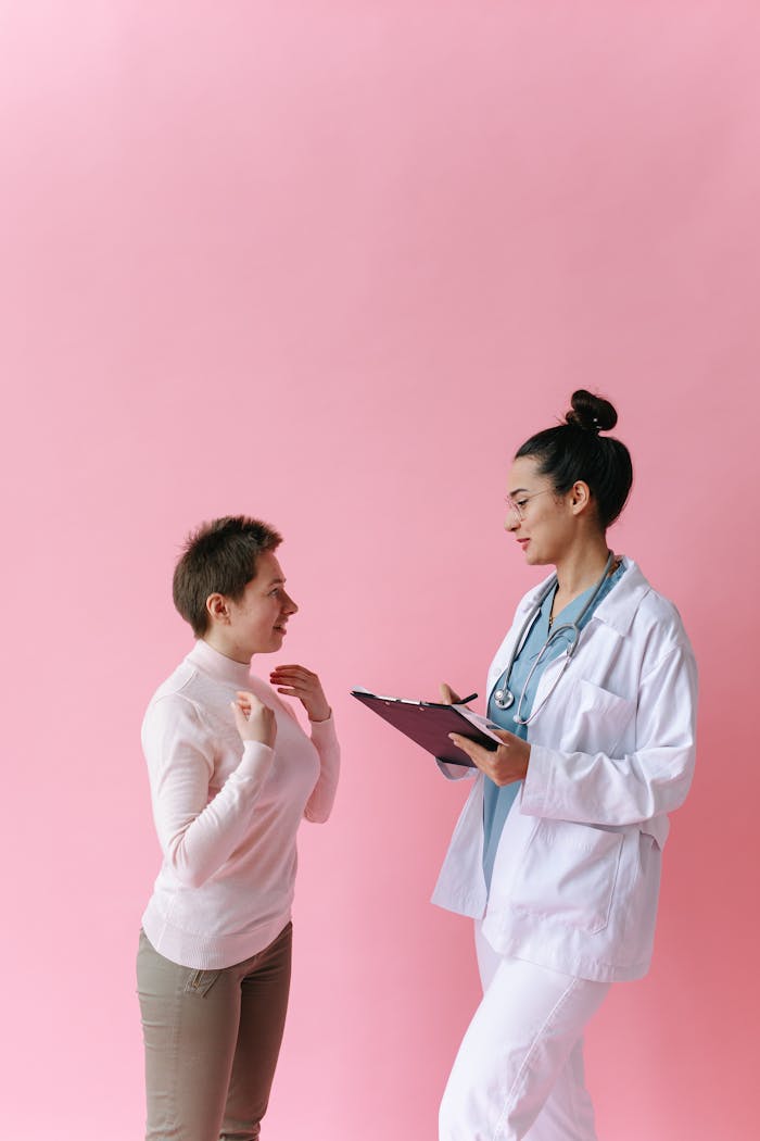 A doctor consults with a patient against a pink background, illustrating healthcare professionalism.