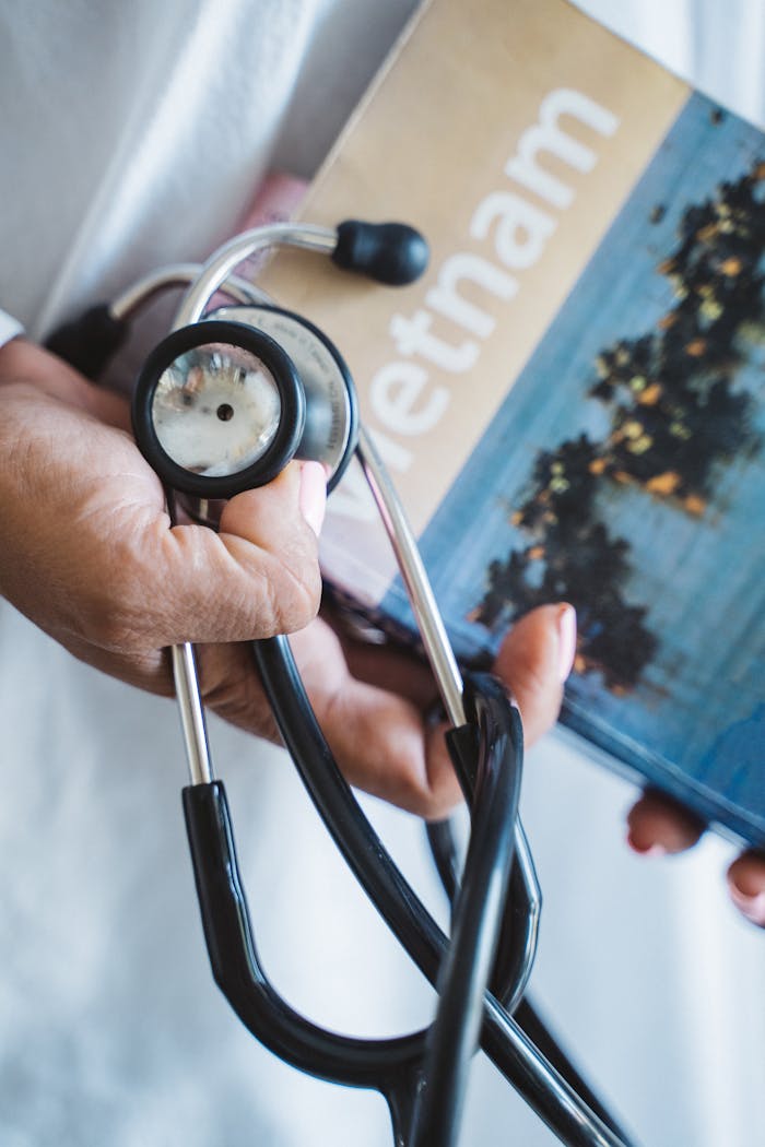 A close-up of a hand holding a stethoscope and a Vietnam travel guide, symbolizing medical care and travel.